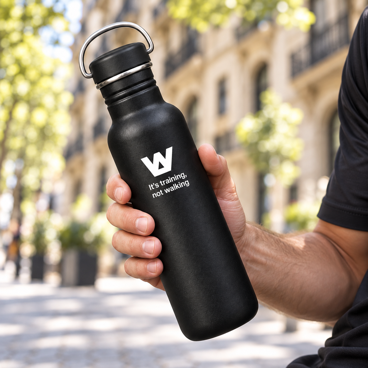 Mano sujetando por el centro una botella negra WalkBCN inclinada en Barcelona
